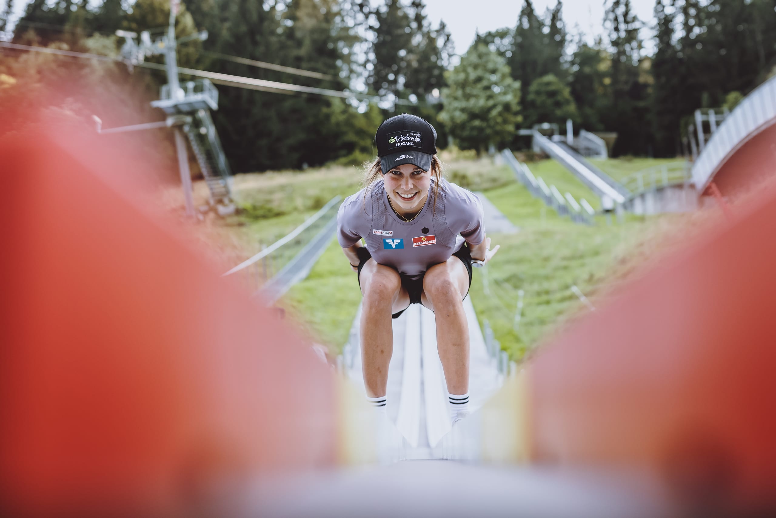 Athletin in der Anfahrtshocke auf der CLUBTRACK-Anlaufspur einer sommerlichen Schanze